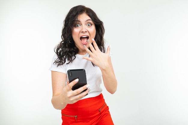 Ragazza bruna sta navigando in Internet con un telefono in mano su uno sfondo bianco isolato.