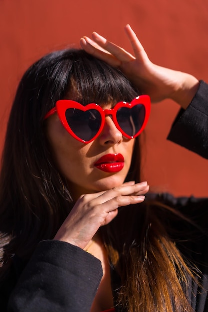 Ragazza bruna su uno sfondo rosso con gli occhiali di cuori san valentino ritratto di una bella ragazza