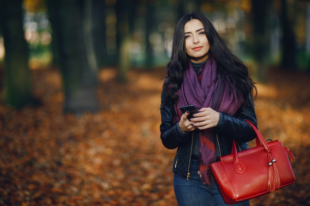 ragazza bruna usando il suo telefono mentre cammina attraverso il parco