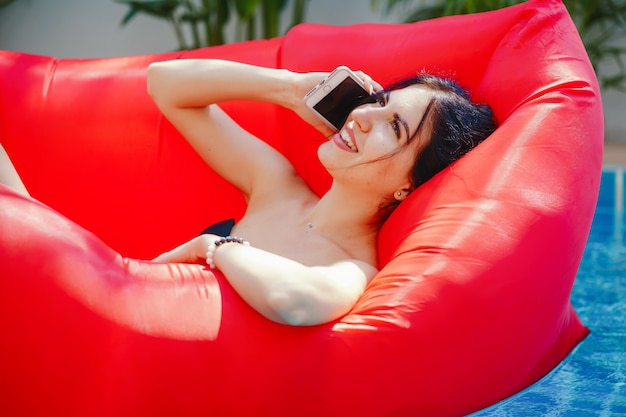 ragazza bruna utilizzando e parlando sul suo telefono mentre galleggia in piscina