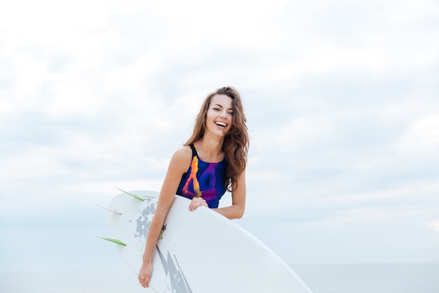 Ragazza bruna vestita in costume da bagno in piedi sull'oceano pronta a fare surf