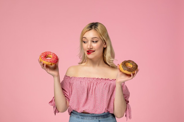 Ragazza carina adorabile bionda pulcino con rossetto rosso in camicetta rosa mordere le labbra guardando le ciambelle