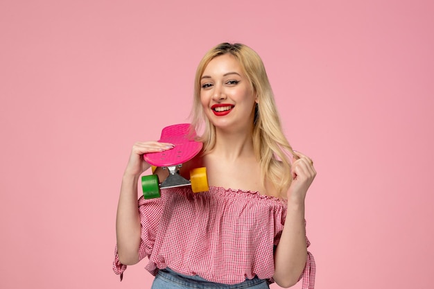 Ragazza carina adorabile pulcino biondo rossetto rosso in camicetta rosa che agisce molto dolcemente con lo skateboard