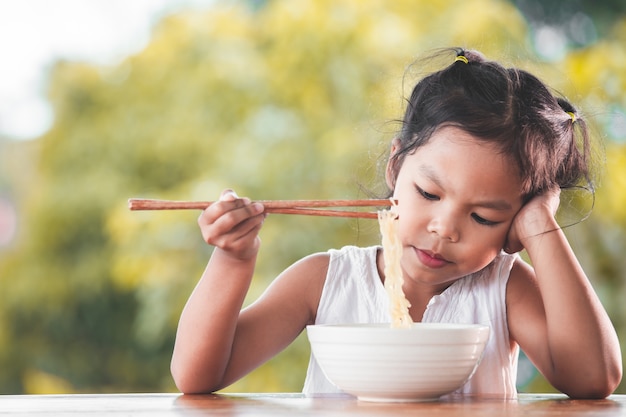 Ragazza carina asiatica bambino annoiato a mangiare spaghetti istantanei per il suo pasto