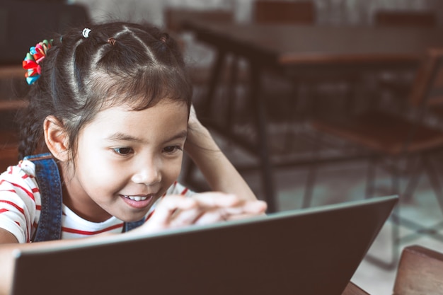 Ragazza carina asiatica bambino utilizzando e giocando sul portatile nel caffè con divertimento e felicità