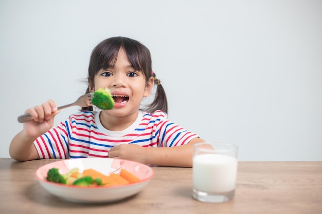 Ragazza carina bambino asiatico mangiare verdure sane e latte per il suo pasto
