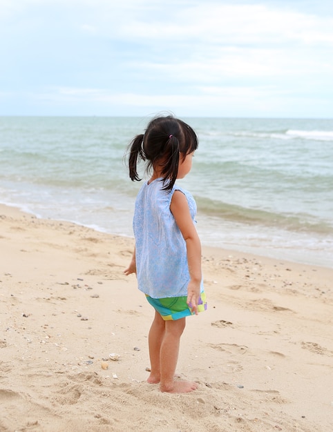 Ragazza carina bambino in piedi sulla spiaggia di sabbia