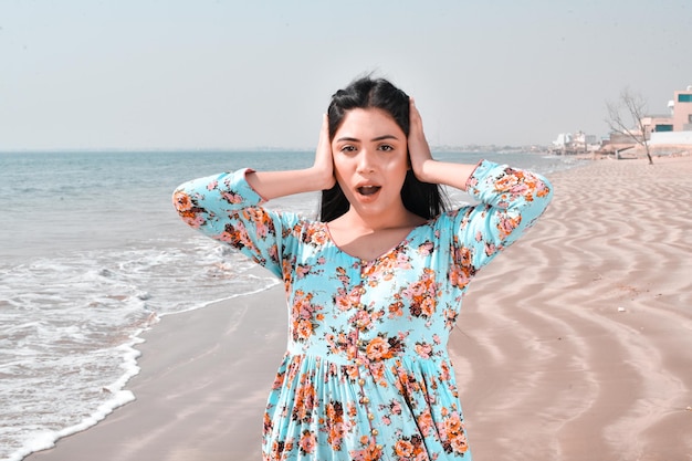 ragazza carina casual entrambe le mani sulle orecchie posano davanti alla spiaggia modello pakistani indiano