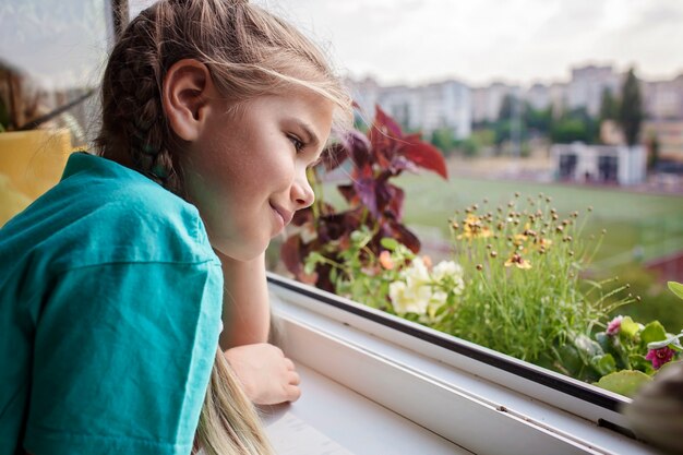 Ragazza carina che aiuta a prendersi cura delle piante domestiche sul concetto dei genitori della pianta della finestra del balcone