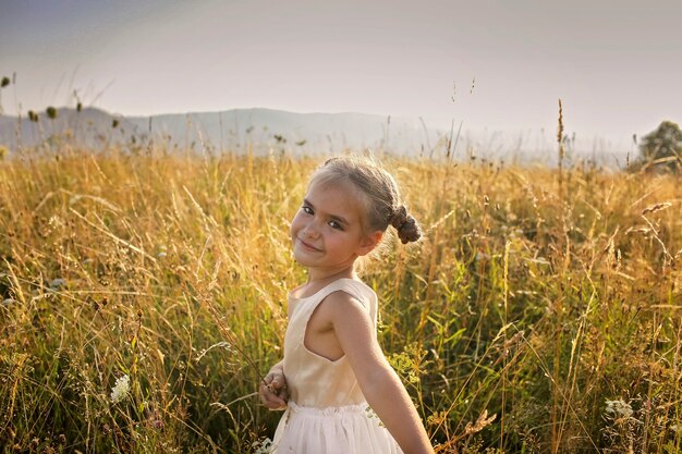 Ragazza carina che balla attraverso un bellissimo prato con grano e fiori in montagna