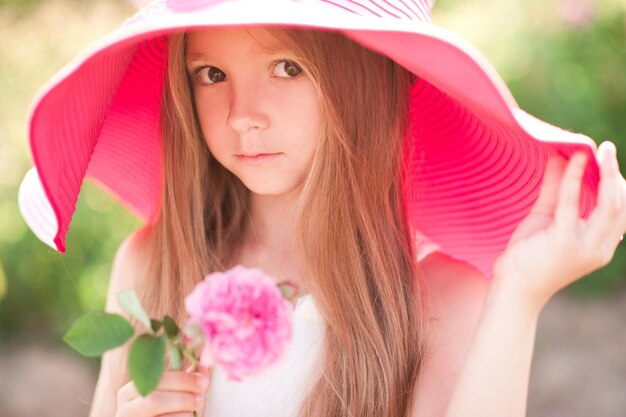 Ragazza carina che indossa un grande cappello rosa che tiene in mano un fiore all'aperto