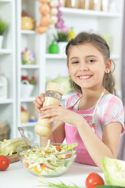 Ragazza carina che prepara una deliziosa insalata fresca in cucina a casa