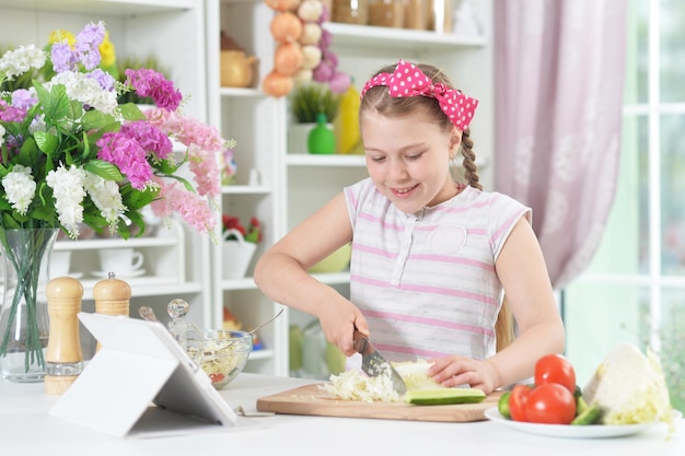 Ragazza carina che prepara una deliziosa insalata fresca in cucina