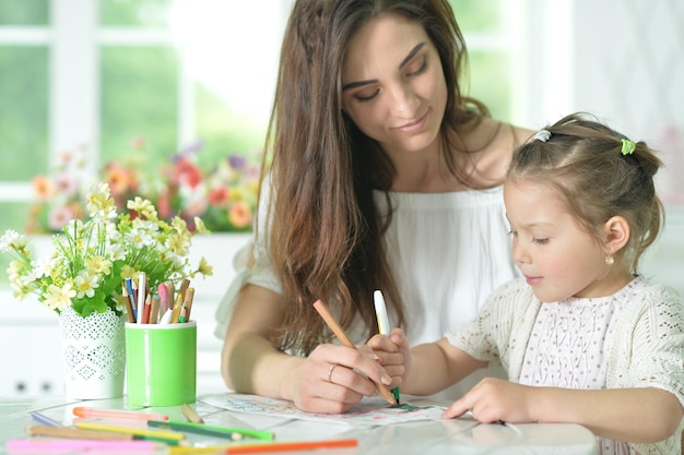 Ragazza carina con la madre che disegna al tavolo