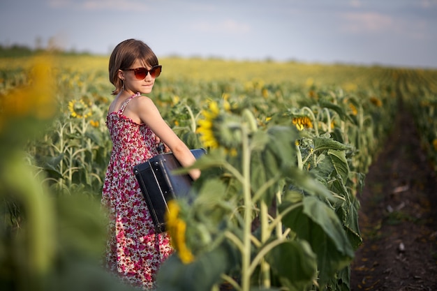 Ragazza carina con la vecchia valigia in un campo di girasoli.