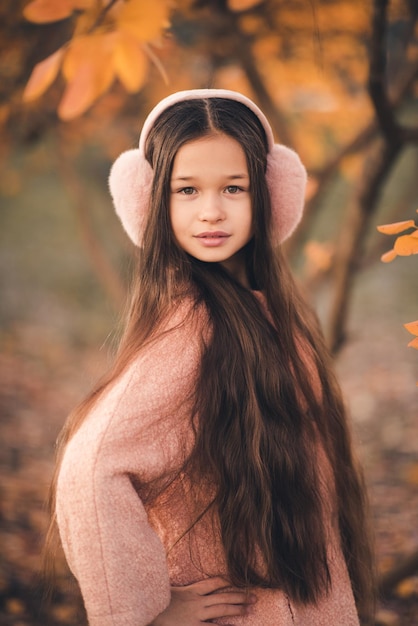 Ragazza carina di 1012 anni con lunghi capelli biondi indossa soffici auricolari ad archetto con foglie autunnali gialle all'aperto Stagione autunnale