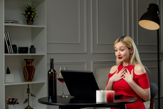 Ragazza carina di amore virtuale in vestito rosso alla data di distanza con il vino che punta a se stessa