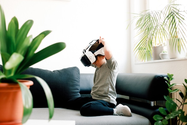 Ragazza carina divertente guardando qualcosa che viene visualizzato negli occhiali di realtà virtuale, seduto sul divano. Concetto di tecnologia moderna