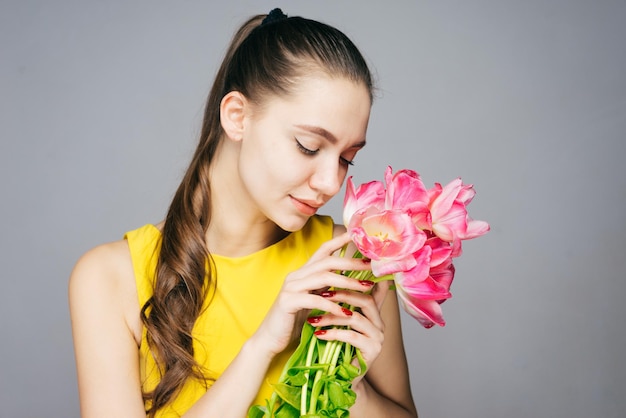 Ragazza carina e carina con un vestito giallo che tiene in mano un mazzo di fiori rosa, godendosi il profumo