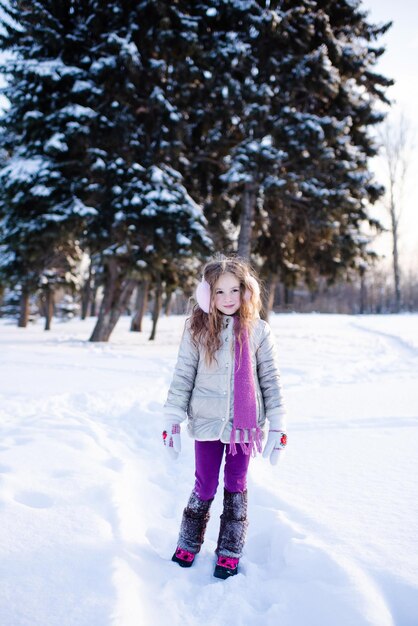 Ragazza carina e divertente che cammina nel parco innevato sullo sfondo della natura all'aperto