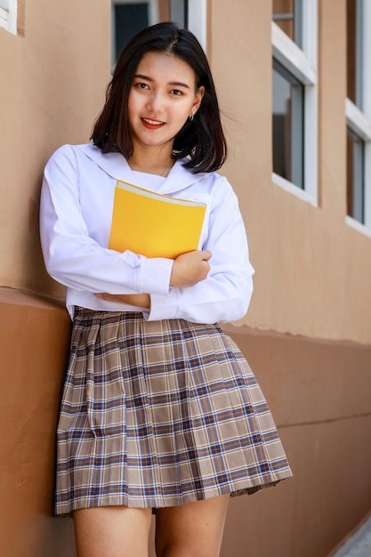 Ragazza carina e giovane che indossa l'uniforme da scolaretta in stile giapponese e coreano che tiene il libro