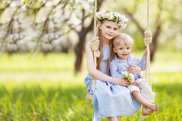 Ragazza carina e ragazzo divertirsi su un'altalena nel vecchio giardino di melo sbocciante. Giorno soleggiato. Attività all'aperto primaverili per bambini