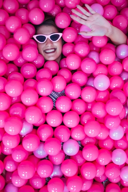 Ragazza carina funky che si diverte in piscina con palloncini di plastica rosa Sfondo di colore rosa isolato