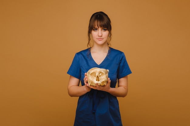 Ragazza carina giovane medico che tiene un cranio umano, sfondo marrone dietro il medico.