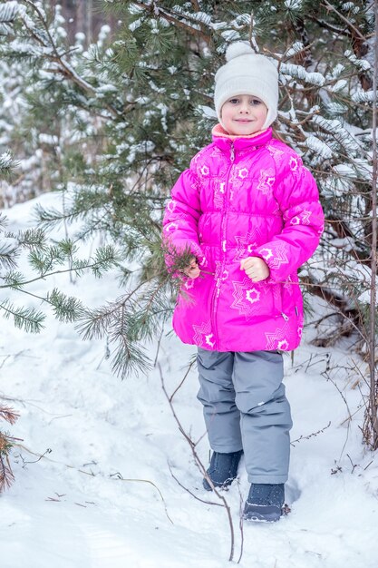 Ragazza carina in abiti caldi rosa che gioca nella foresta invernale, trascorrendo del tempo all'aperto in inverno