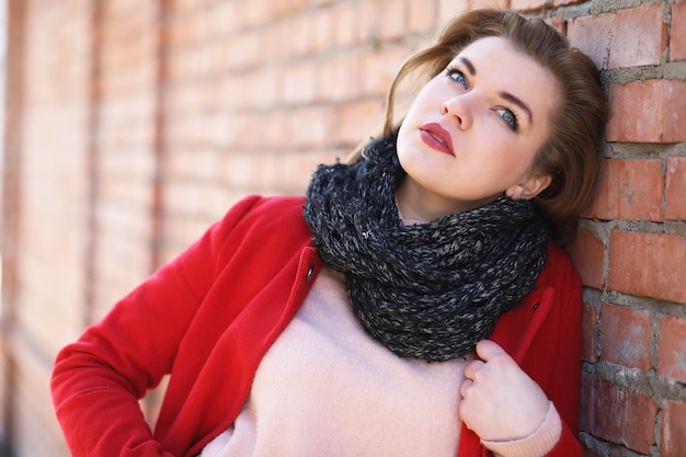 Ragazza carina in cappotto rosso su sfondo muro di mattoni