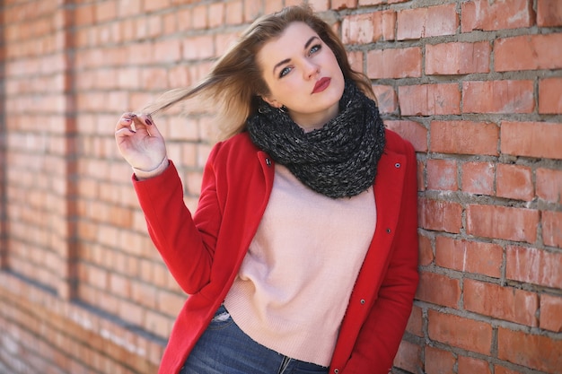 Ragazza carina in cappotto rosso su sfondo muro di mattoni