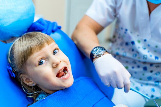 Ragazza carina in clinica dentale. Bambino in gabinetto stomatologico a bocca aperta.