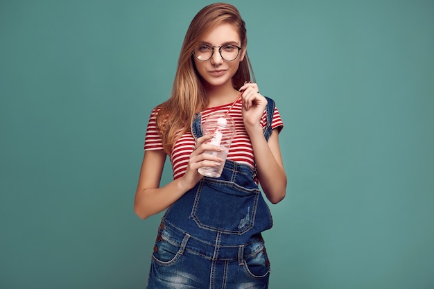 Ragazza carina in tuta di jeans e bicchieri con selz