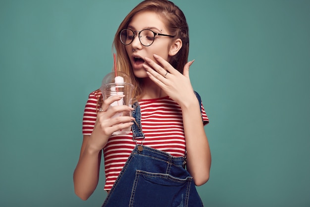 Ragazza carina in tuta di jeans e bicchieri con selz