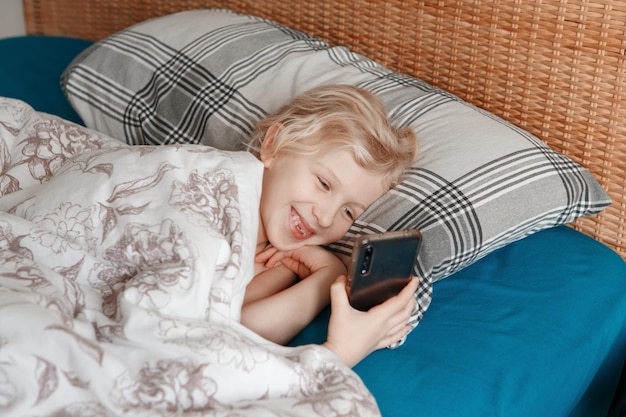 Ragazza carina sdraiata a letto la mattina e che manda messaggi, che parla sui social media con lo smartphone.
