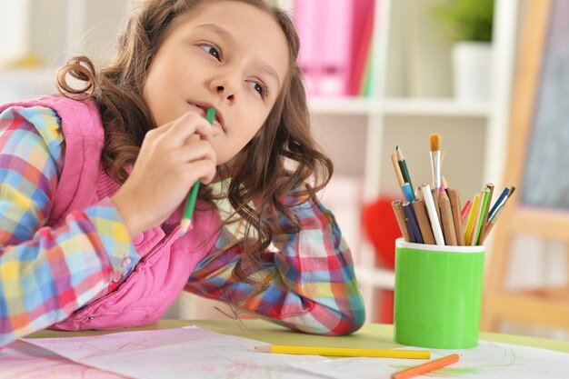 Ragazza carina seduta a tavola e disegnando a casa