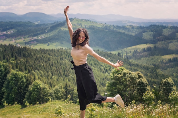 Ragazza carina sta saltando sullo sfondo di montagne e foreste