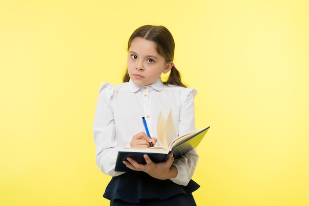 Ragazza carina studentessa in uniforme tenere libro con informazioni sfondo giallo Allievo ottenere informazioni dal libro Abbigliamento bambino uniforme scolastica prepararsi per le informazioni sulla lezione Notare le informazioni