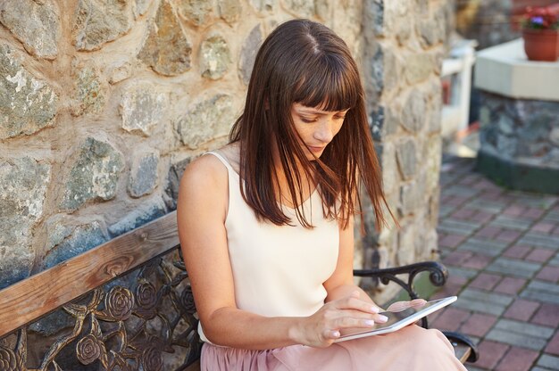 Ragazza carina utilizzando una tavoletta in panchina all'aperto