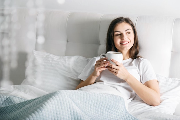 Ragazza castana che beve caffè al letto