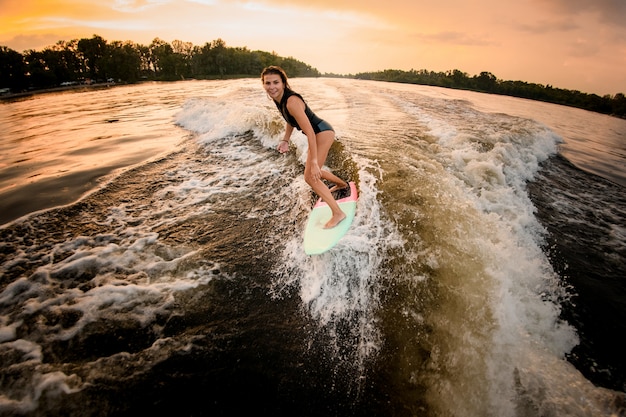 Ragazza castana che guida sul wakeboard sul fiume sull'onda del motoscafo