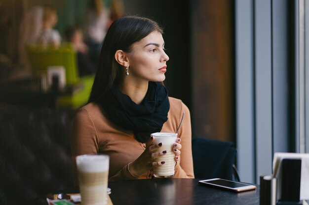 ragazza castana che utilizza il suo telefono mentre bevendo caffè ad un ristorante