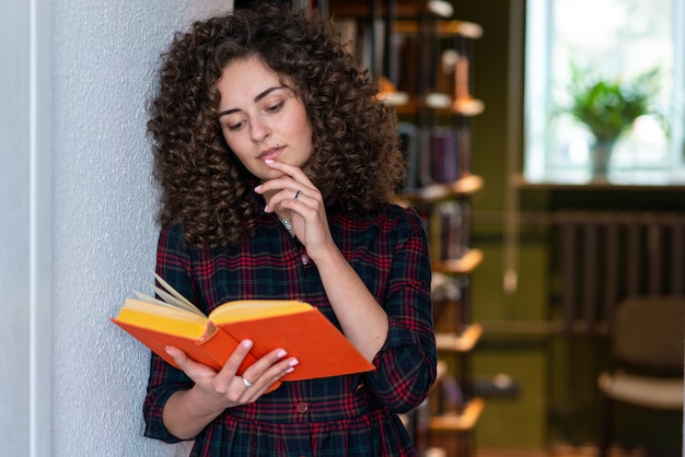 Ragazza castana riccia che tiene un libro in sua mano