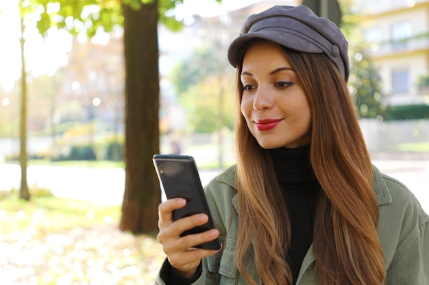 Ragazza casuale che porta cappello e collo di polo che digita sullo smartphone all'aperto