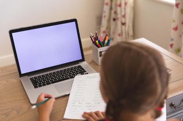 Ragazza caucasica che ha videochiamata durante la lezione su laptop con spazio per la copia, seduta alla scrivania a casa