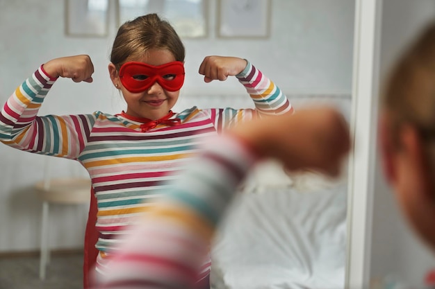 Ragazza caucasica che indossa un costume di supereroe accanto allo specchio