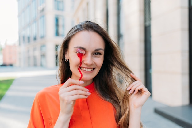 Ragazza caucasica che sorride flirta con un accessorio a forma di cuore che cammina per la città