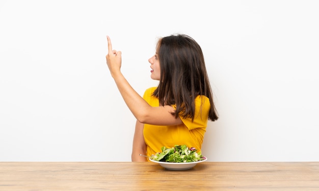 Ragazza caucasica con insalata che indica indietro con il dito indice