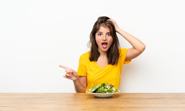 Ragazza caucasica con insalata sorpresa e puntando il dito verso il lato