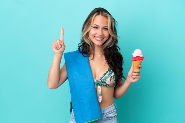 Ragazza caucasica dell'adolescente che tiene il gelato e l'asciugamano isolati su fondo blu che indica una grande idea